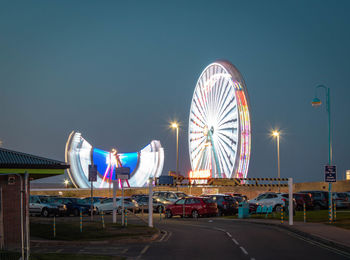 Illuminated ferris wheel against sky in city at night