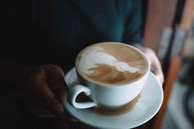 Close-up of hand holding cappuccino served on table