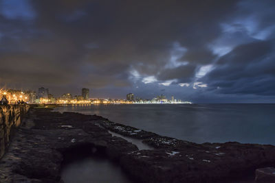 Scenic view of sea by illuminated city against sky