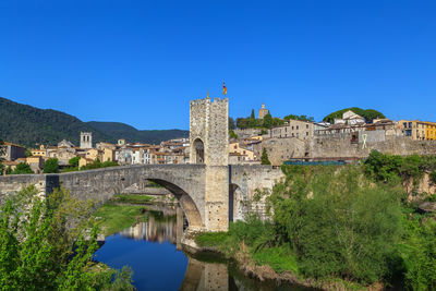 Buildings by lake against clear blue sky