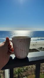 Midsection of man holding drink at beach against sky