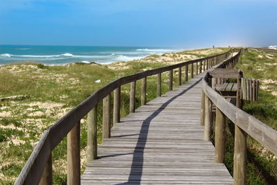 Footbridge leading towards sea against sky