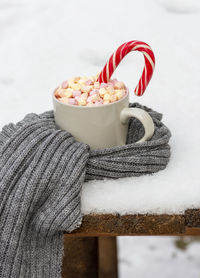 Close-up of marshmallows and candy cane in coffee cup on snow during winter