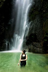 Portrait of young woman standing by waterfall