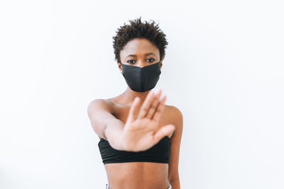 Beautiful young african american woman in black top and face mask on white, stop coronavirus 