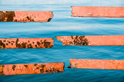 Close-up of rusty metal grate against blue water