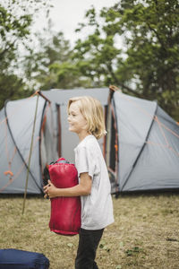 Side view of smiling boy holding tent while standing against tent