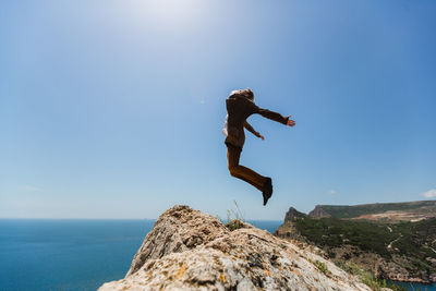 Man jumping on rock by sea against clear sky