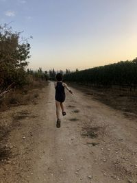 Rear view of man running on dirt road against sky