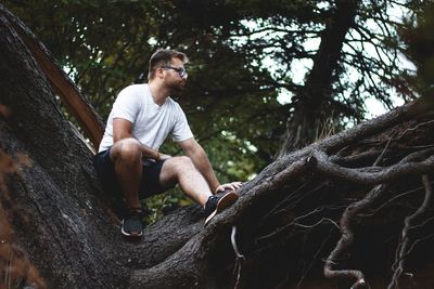Full length of young man sitting on tree trunk