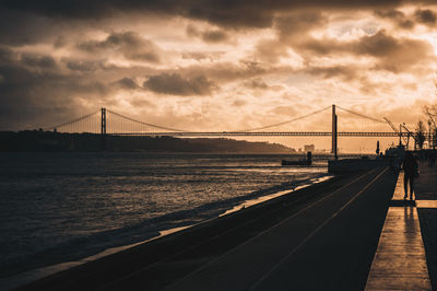 Suspension bridge over river against cloudy sky