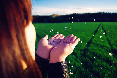 Young woman blowing flower petals on grassy field