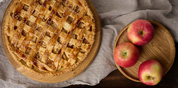 Round baked apple pie on a brown wooden table, top view