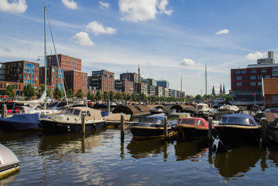 Boats moored at harbor by buildings against sky