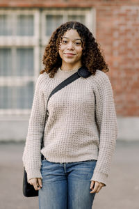 Portrait of smiling female teenage student with curly hair standing in high school campus