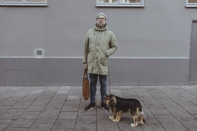 Full length of mid adult man standing with dog against building in city