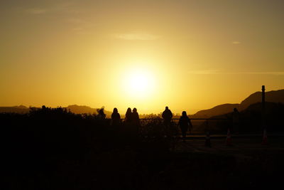 Silhouette people on field against sky during sunset