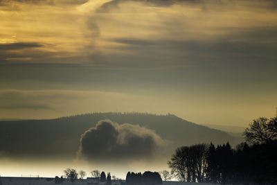 Silhouette trees against dramatic sky during sunset