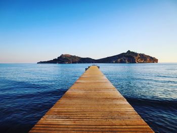 Pier over sea against clear blue sky