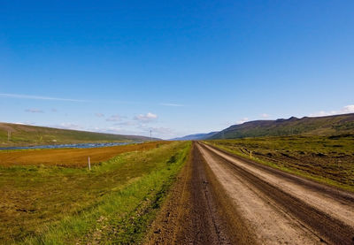 Road amidst field against clear blue sky