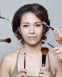 Portrait of mid adult woman holding make-up equipment against gray background