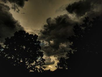 Low angle view of silhouette trees against storm clouds