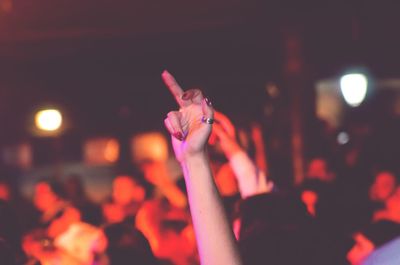 Cropped hand of female fan showing obscene gesture during music festival at night