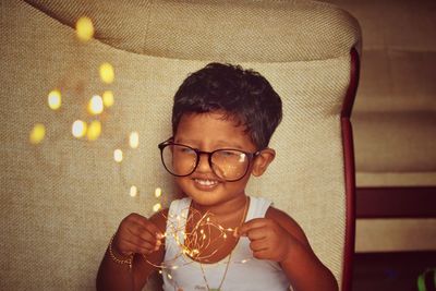 Cute boy with string lights sitting on sofa