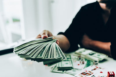 Midsection of businessman holding us paper currency while playing cards on table