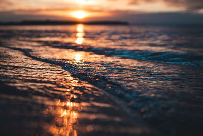 Small waves breaking onto the beach reflecting the sunset.