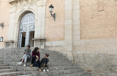 Mother sitting with daughter on steps against historical building