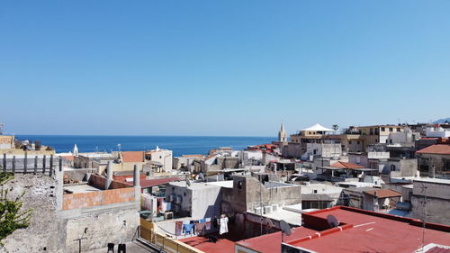 Townscape by sea against clear blue sky