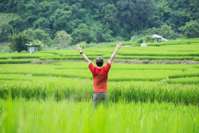 Rear view of man with arms outstretched standing on field