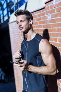 Smiling man listening music while standing by brick wall