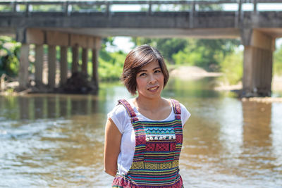 Portrait of smiling woman standing in river against bridge