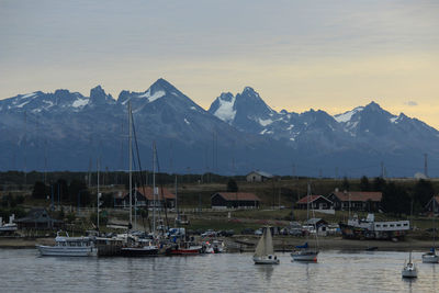 Sailboats moored on river by snowcapped mountains against sky