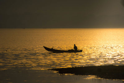 Silhouette man in boat on sea against sky during sunset