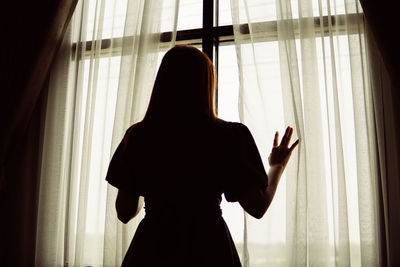 Rear view of woman looking through window at home