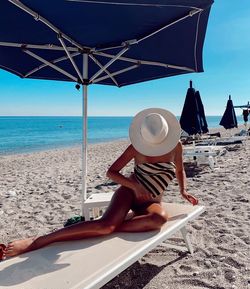 Woman covering face with hat while sitting on seat at beach