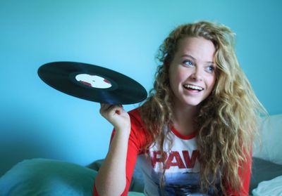 Cheerful woman holding record while sitting on bed at home