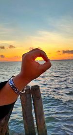 Person hand on sea against sky during sunset