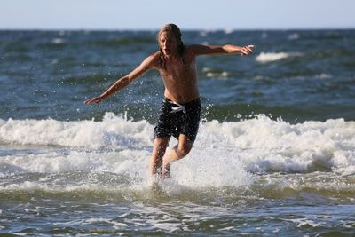 Playful shirtless man at beach with arms outstretched