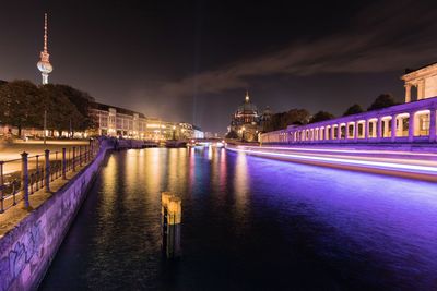 Light trails on river amidst buildings at night