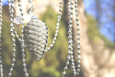 Gray christmas tree toy pine cone with silver beads hang on a natural background in haze close up