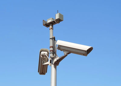 Low angle view of surveillance cameras against blue sky