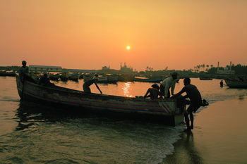 Men pulling out fishing boat in sea at sunset