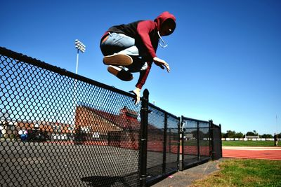 Low angle view of man jumping over fence