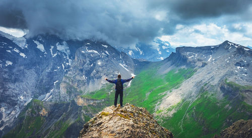 Rear view of man standing with arms outstretched against mountains