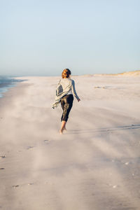 Rear view of young woman walking at beach against clear sky during sunset