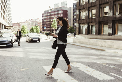 Businesswoman looking at smart phone while crossing street